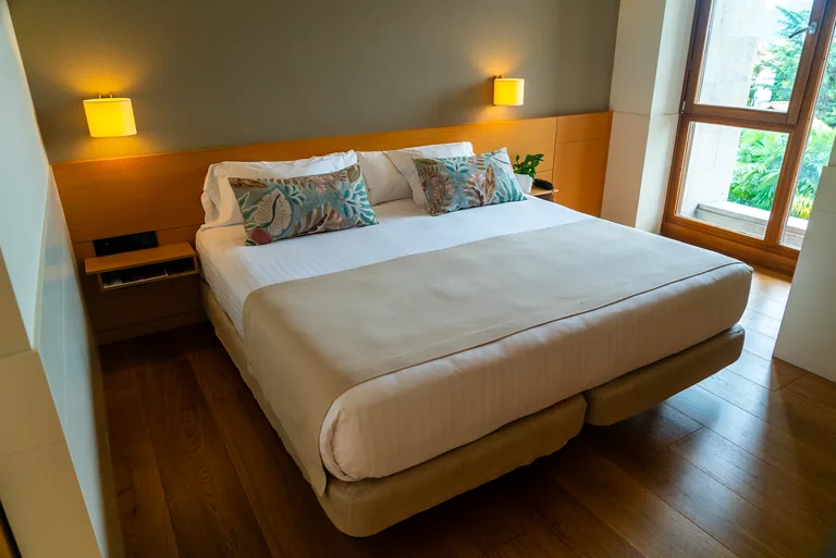 Habitación con la cama hecha y el ventanal abierto al jardín